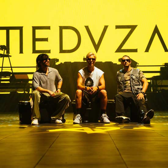 Three MEDUZA members seated in front of a yellow MEDUZA backdrop