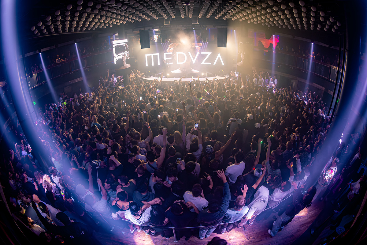 An elevated view across District Atlanta's packed main room toward the illuminated stage beneath rows of suspended spheres